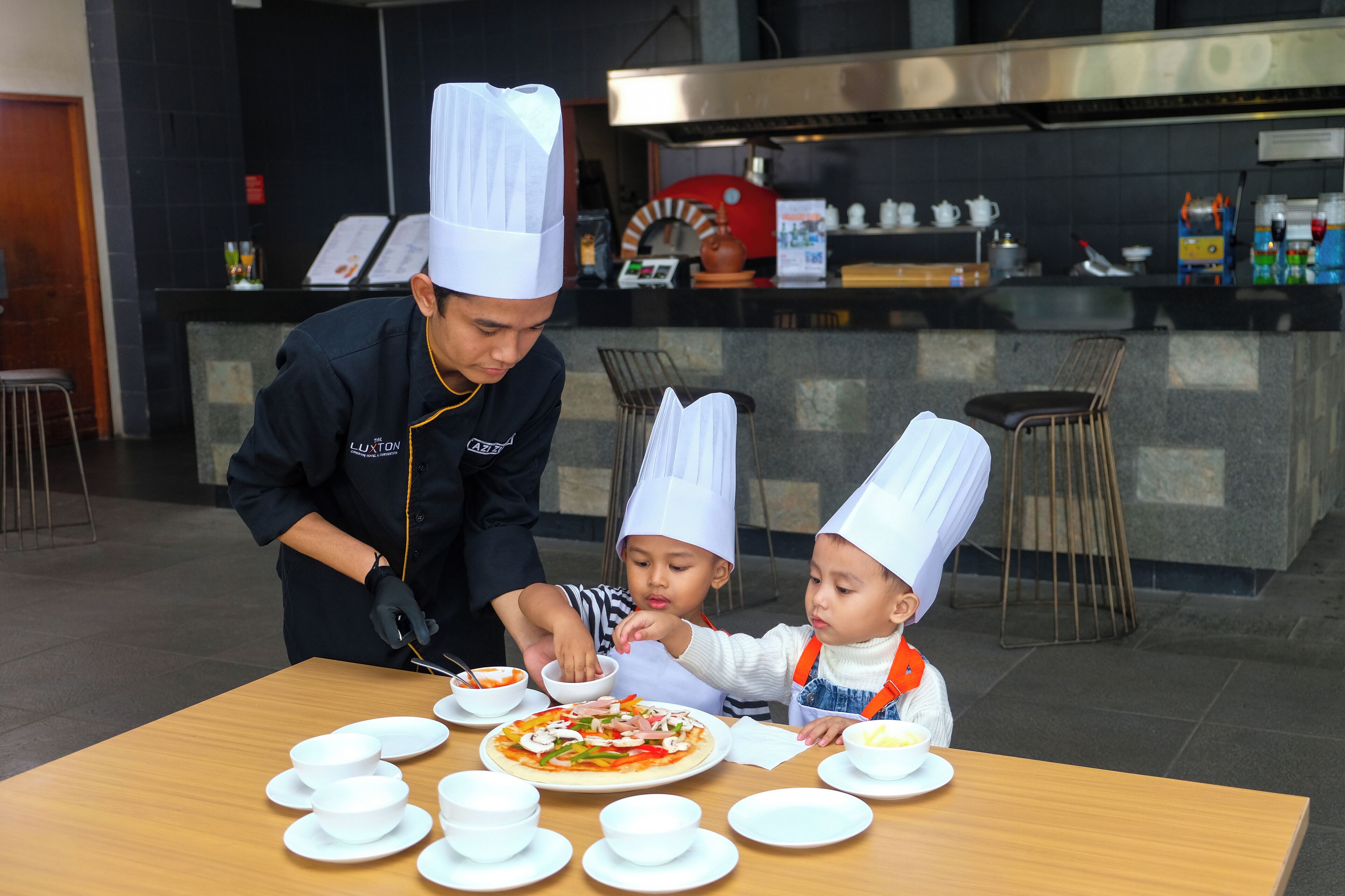 A chef and two children at a table with a pizza and bowls.