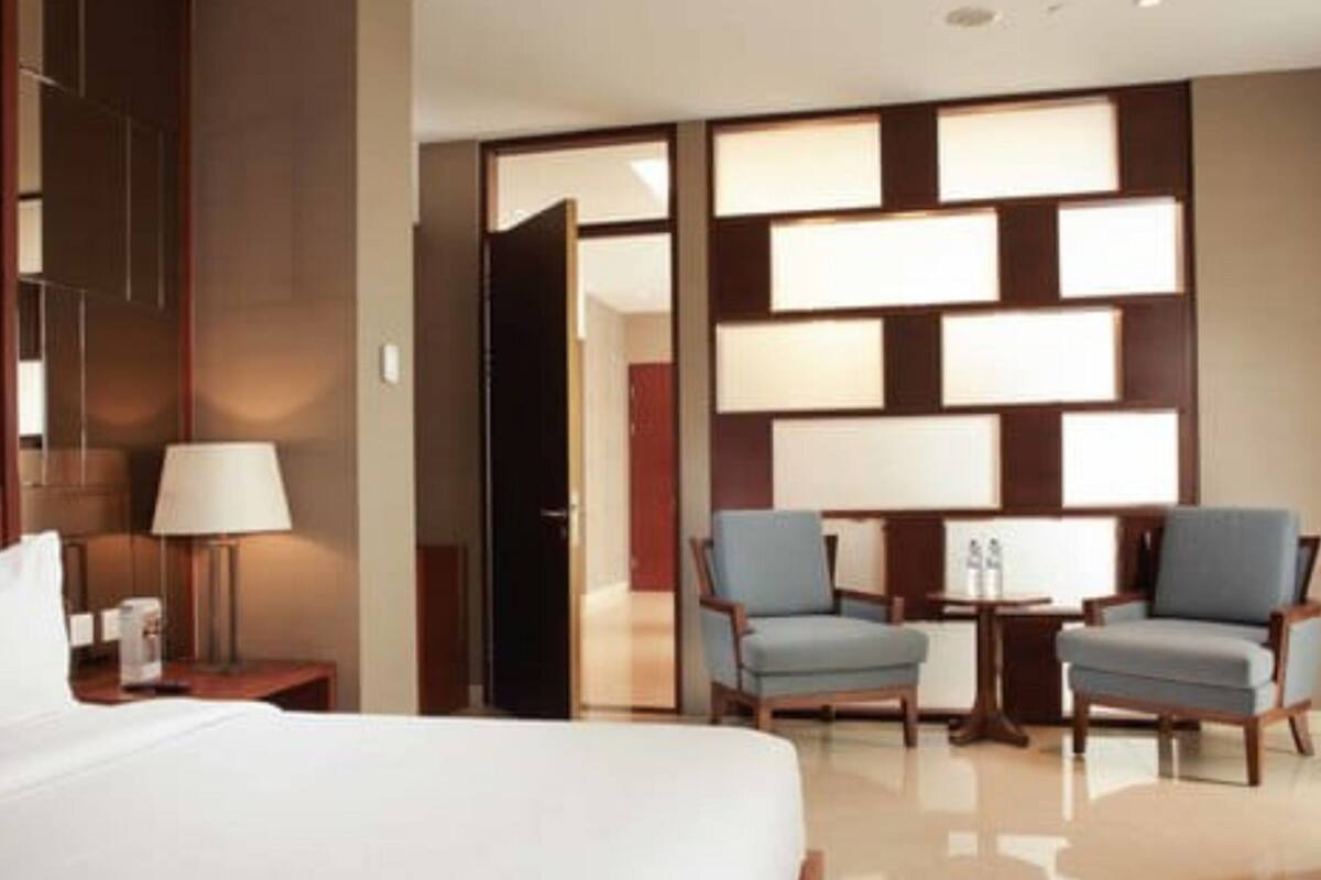 Habitación de hotel con una cama grande, dos sillones, una mesita y una pared con paneles rectangulares.