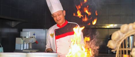 A chef in a white uniform with a red stripe, cooking with a large flame.