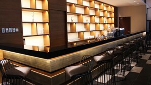 Un bar moderno con una barra larga, distintas opciones de asientos y estanterías con copas.