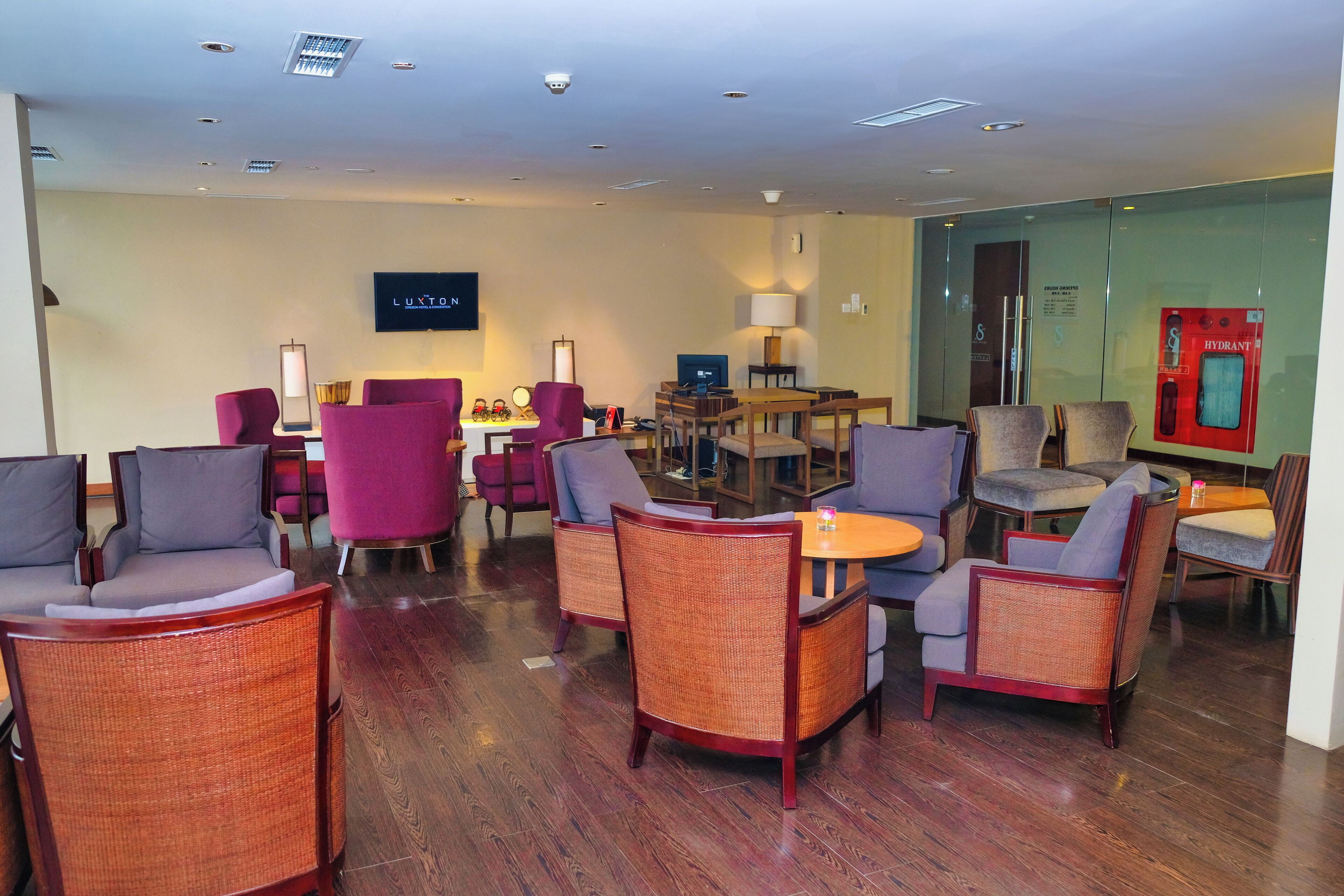 A hotel lobby with wicker chairs, a flat-screen TV, and a fire extinguisher.