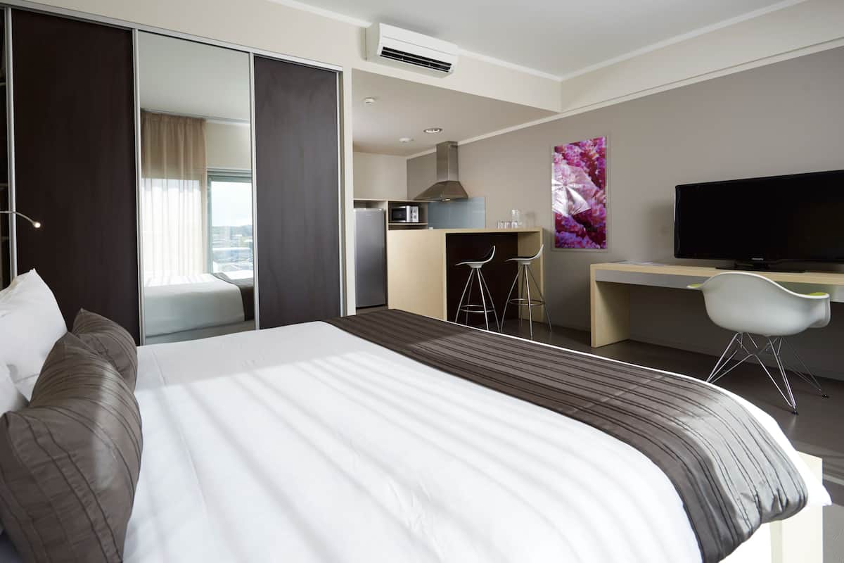 A modern hotel room with a large bed, a desk, a television, and a view of the city through the window.