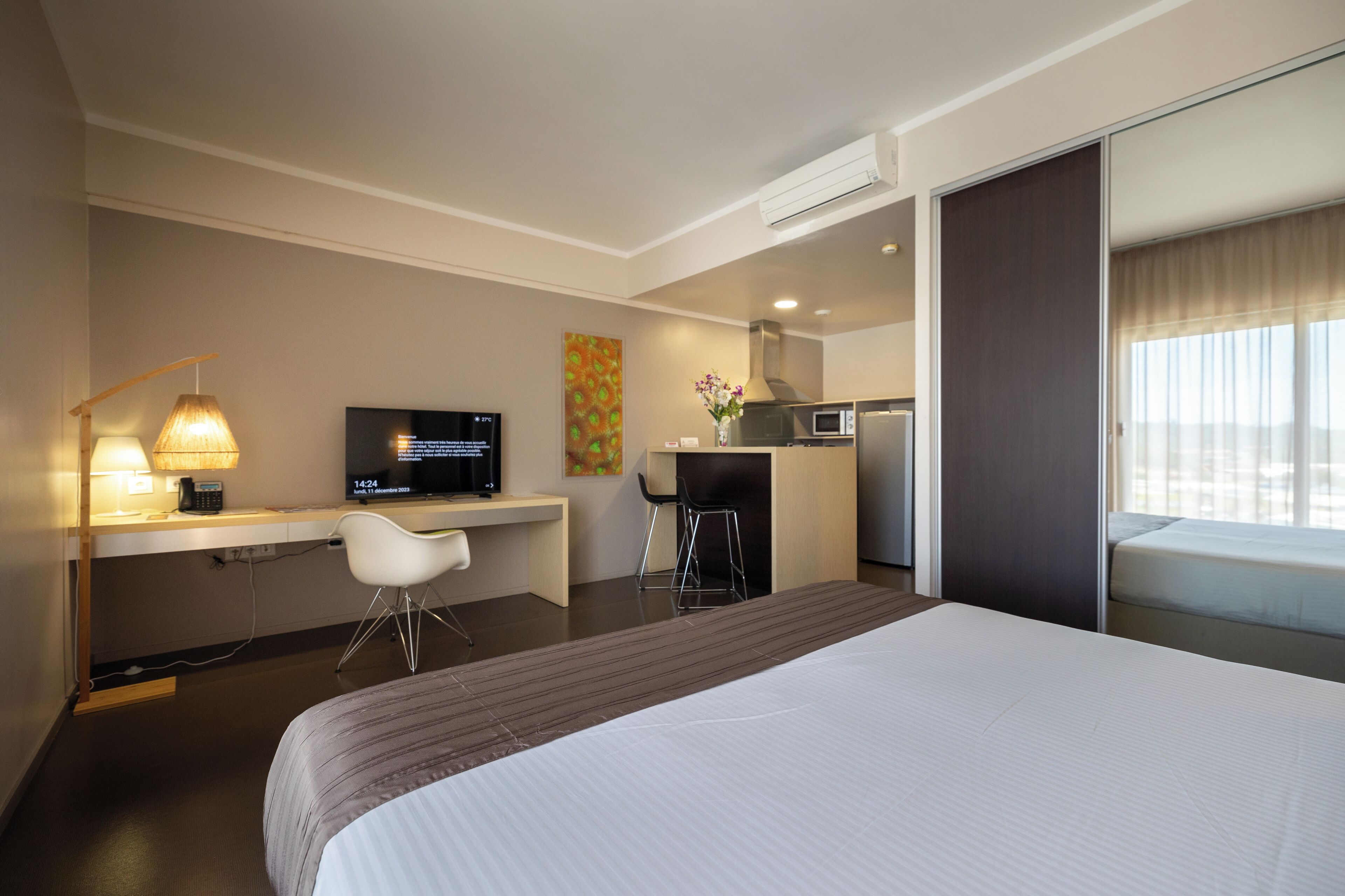 Habitación de hotel con cama, escritorio, silla, televisor y kitchenette.