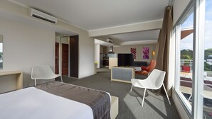 A hotel room with a bed, two chairs, a desk, a TV, and a balcony with a view. - L'Hôtel du Centre (Nouméa)