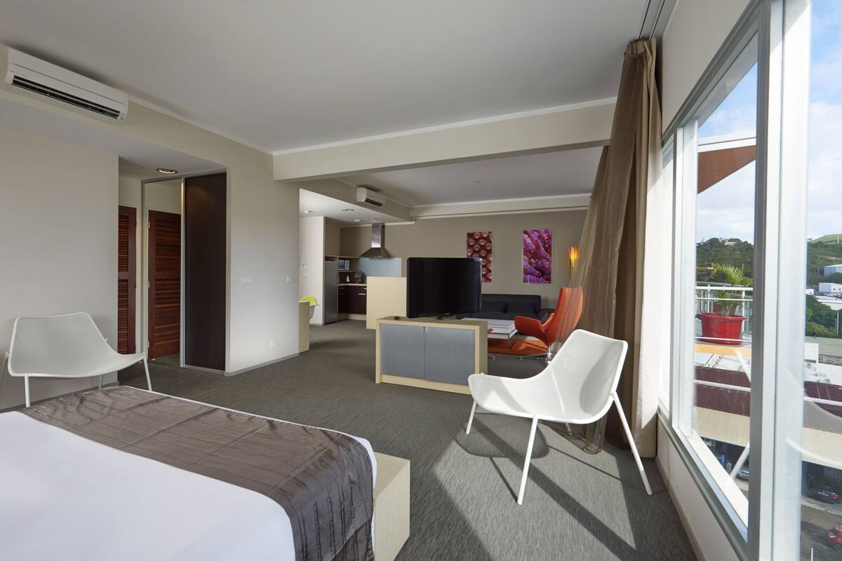 A hotel room with a bed, two chairs, a desk, a TV, and a balcony with a view.