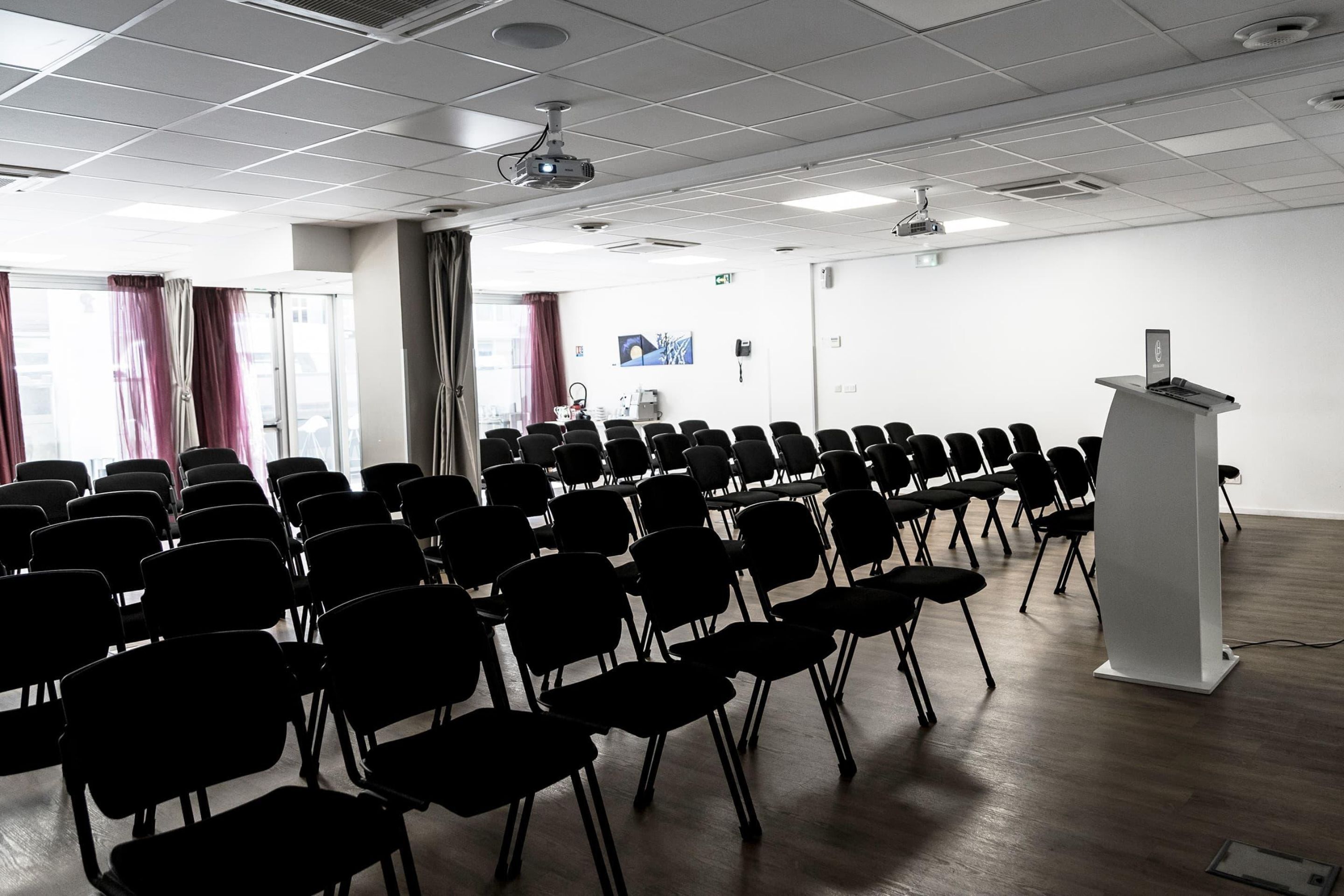 A conference room with rows of chairs, a podium, and a projector on the ceiling.