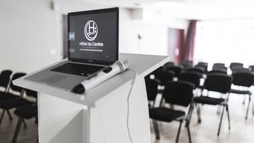 A laptop on a podium with a logo and text "Hôtel du Centre" in a conference room with rows of chairs.