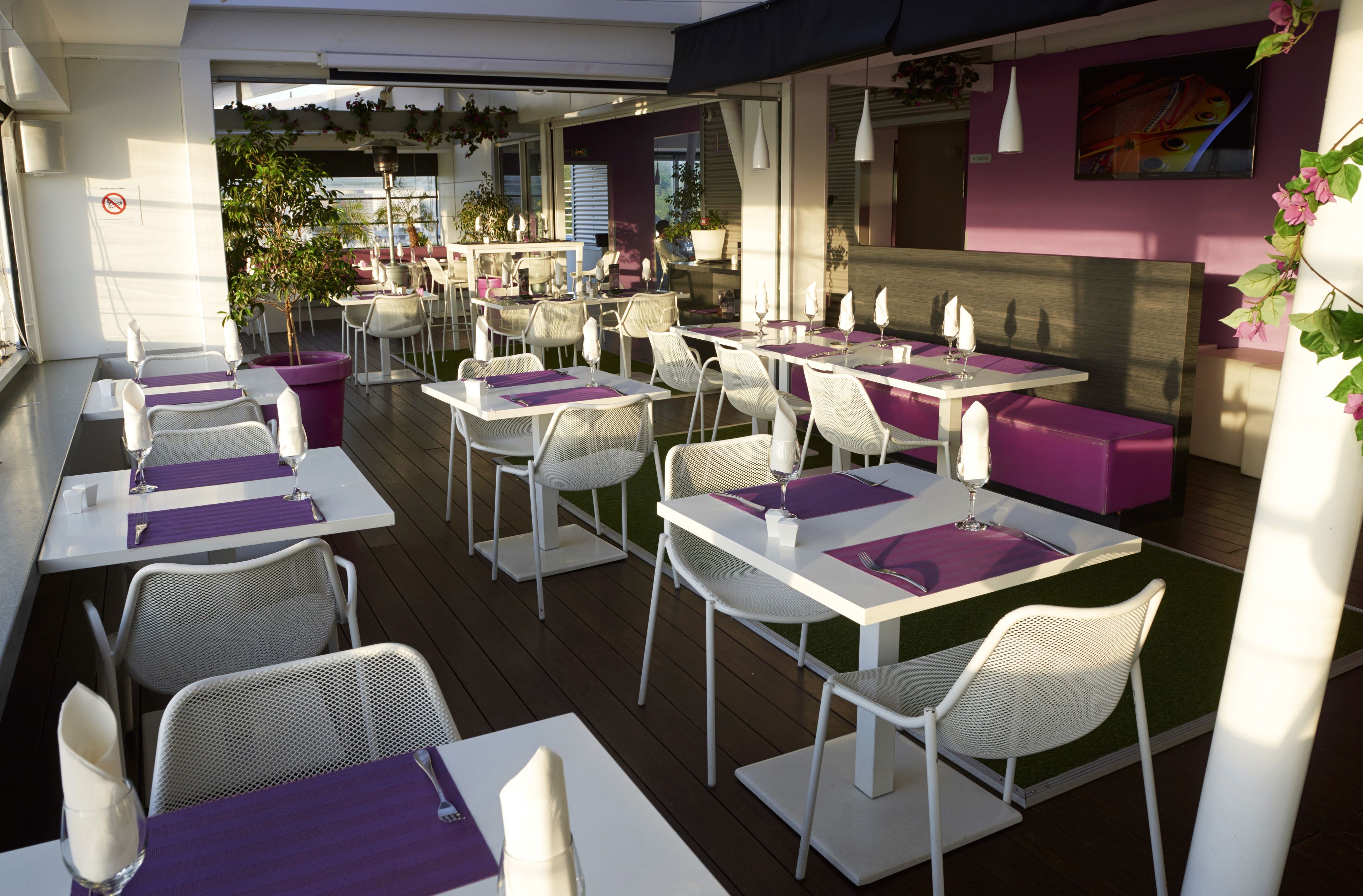 An outdoor dining area with white tables and chairs, purple table runners, and potted plants.