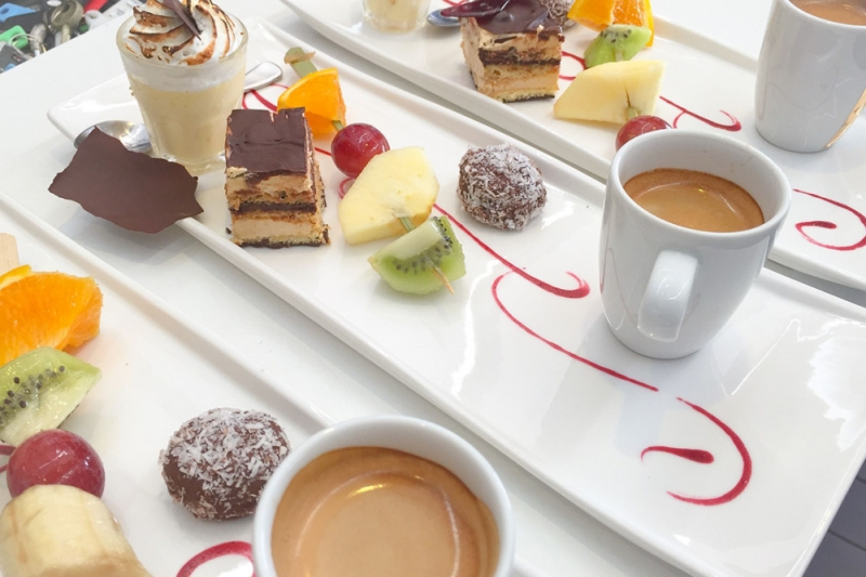 A white tray with various desserts, fruits, and a cup of coffee.
