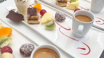 A white tray with various desserts, fruits, and a cup of coffee.