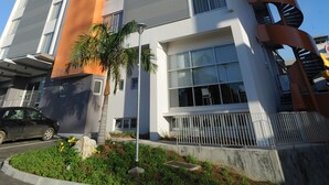 A modern multi-story hotel with a distinctive orange and grey facade, large windows, and a spiral staircase on the right side. - L'Hôtel du Centre (Nouméa)