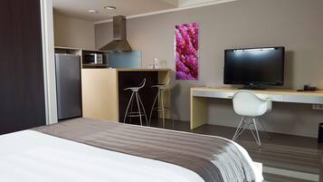 A hotel room with a bed, a desk with a television, a microwave, and a refrigerator.