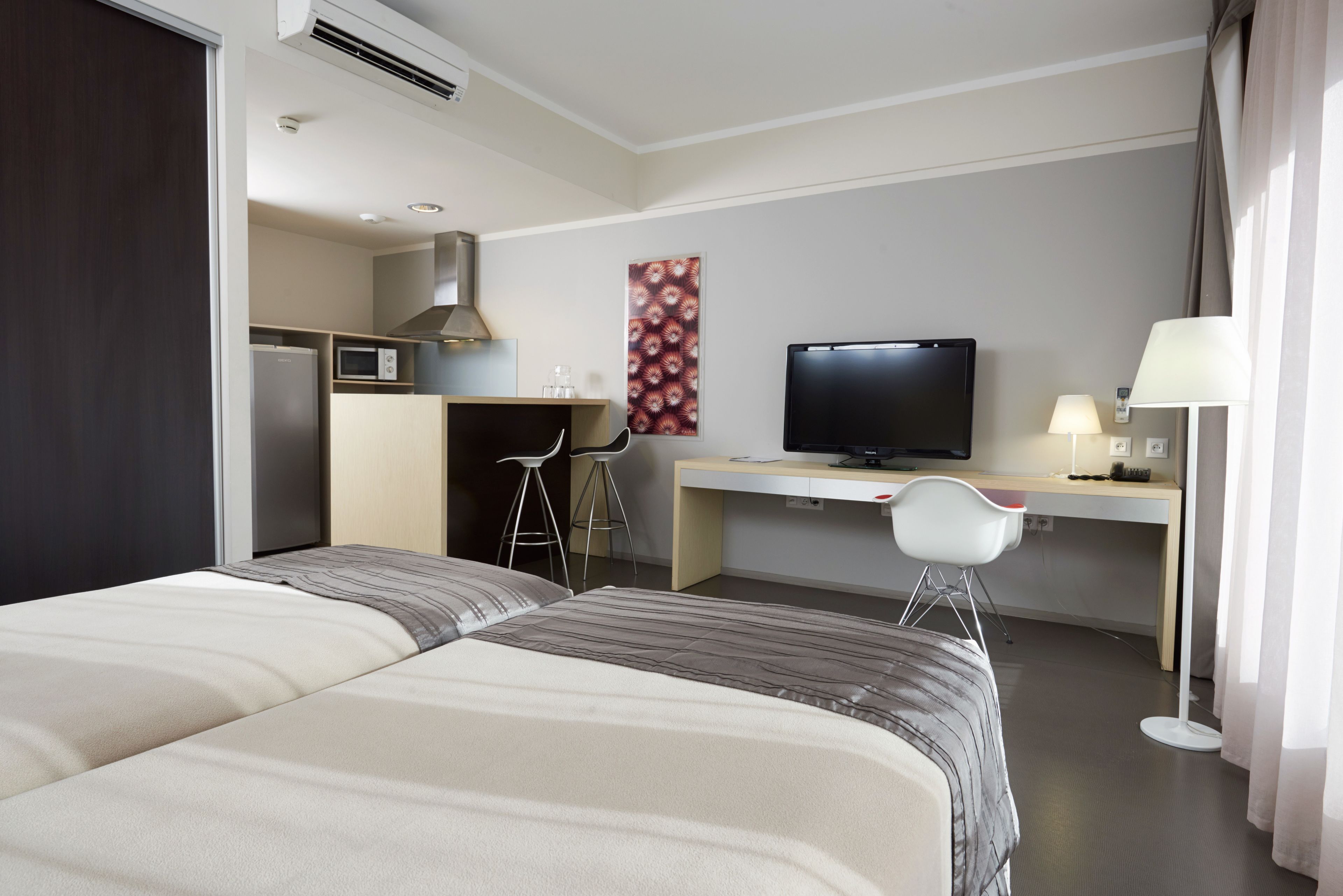 Habitación de hotel con dos camas, un escritorio, un televisor, una lámpara y una kitchenette.