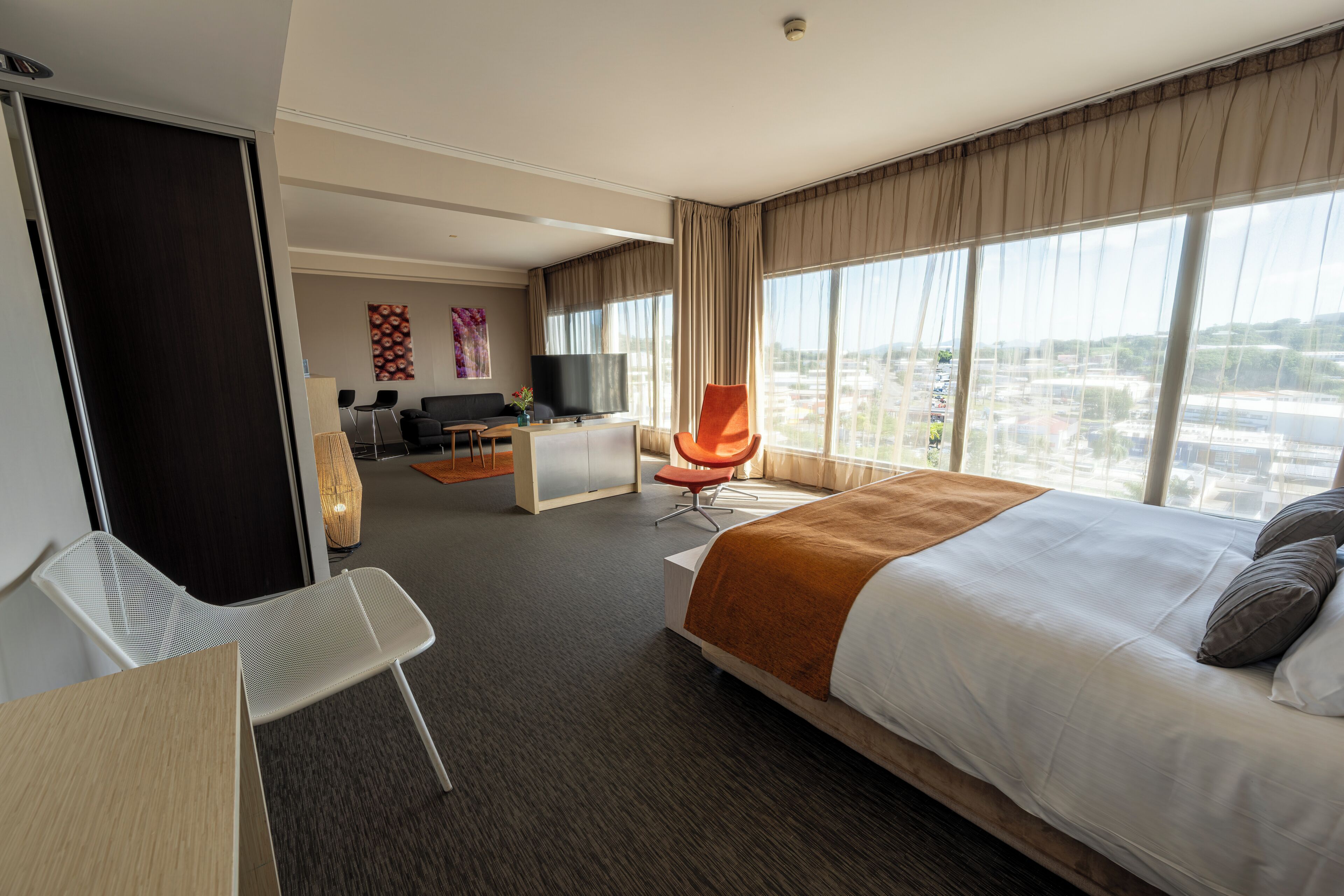 A hotel room with a large bed, a desk, a chair, a television, and a view of the city.