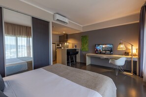 Habitación de hotel con cama, escritorio, silla, televisor y kitchenette.