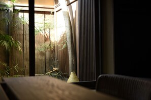 Ein Zimmer mit Holzboden, einer Couch, einem Tisch und einem Fenster mit Blick auf einen Bambusgarten.