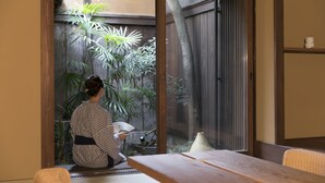 A room with tatami flooring, a low wooden table, and a sliding glass door leading to a garden with plants and a small pond. - Kuraya Kiyomizu-Gojo (Kyoto)