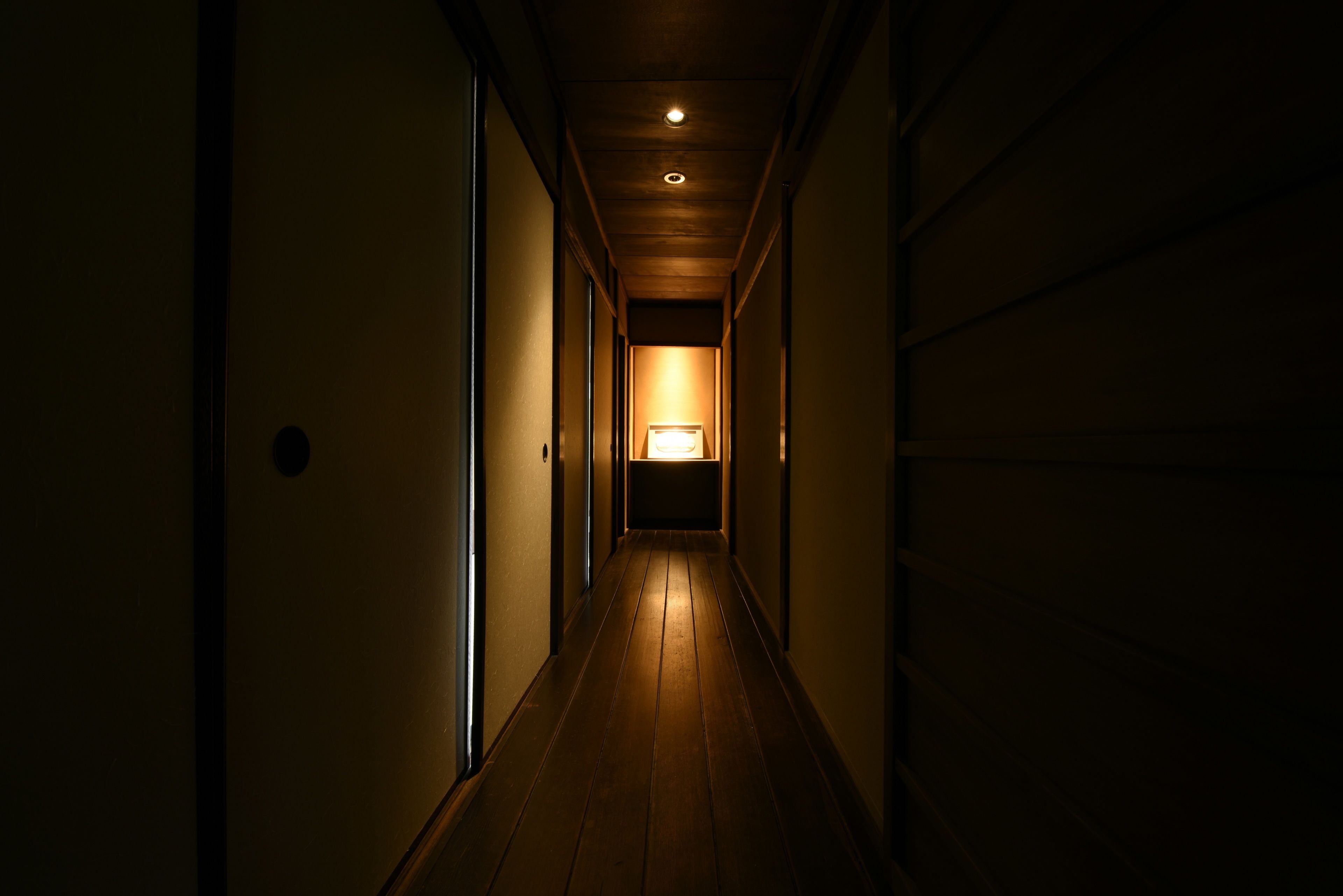 A narrow hallway with wooden flooring and a single light source at the end.