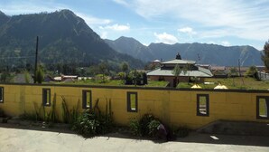 A yellow wall with windows, a building with a green roof, and mountains in the background. - Yog Bromo Homestay (Ngadisari)