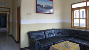 A living room with a black leather sofa, a framed picture on the wall, a window with wooden frames, and a door leading to another room. - Yog Bromo Homestay (Ngadisari)
