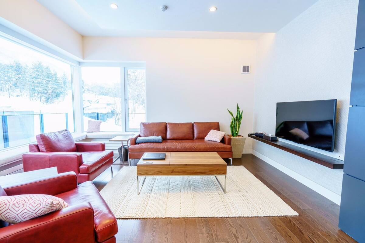 A modern living room with a brown leather sofa, a wooden coffee table, and a flat-screen TV mounted on the wall.