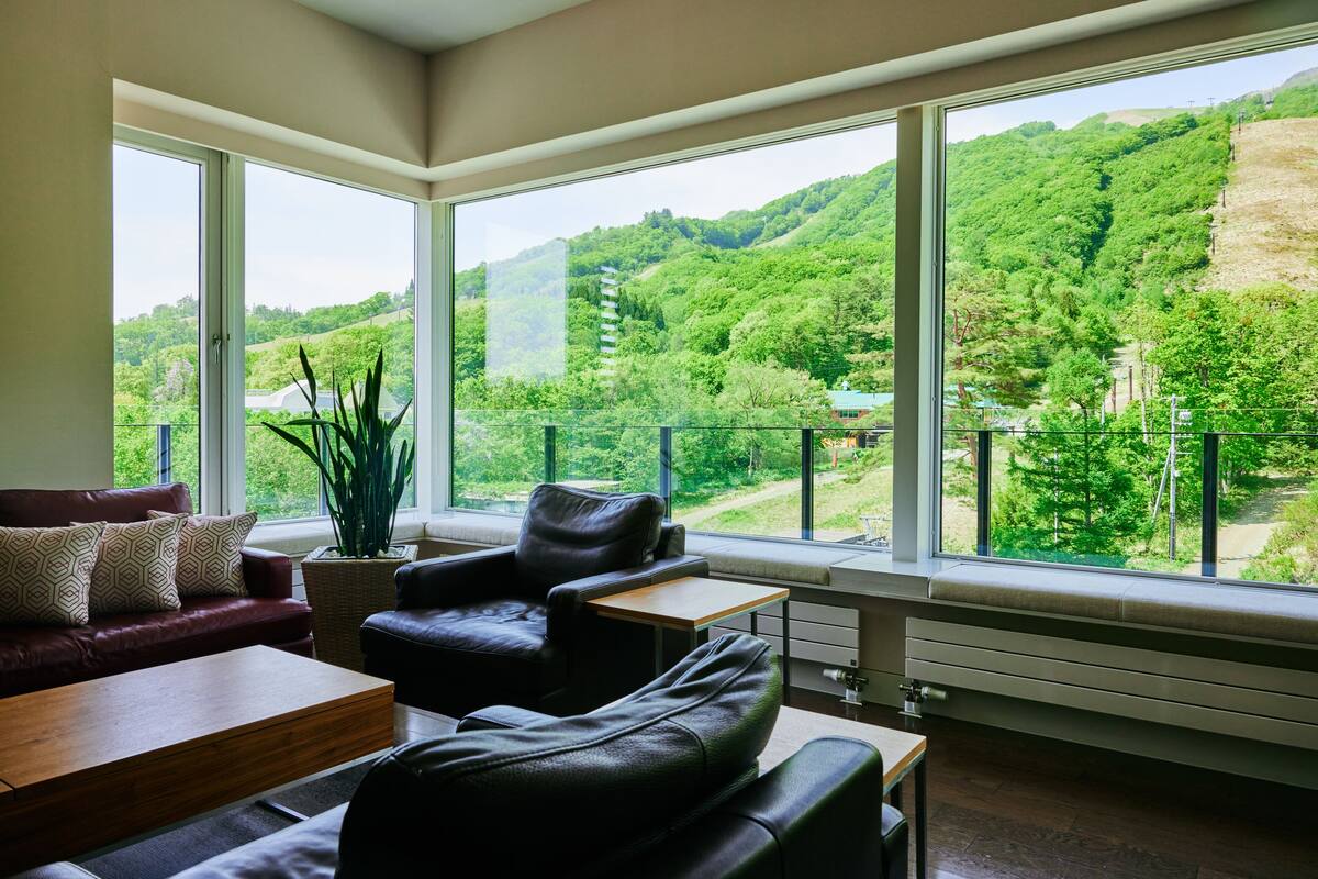 A modern living room with a large window offering a view of a lush green hillside.