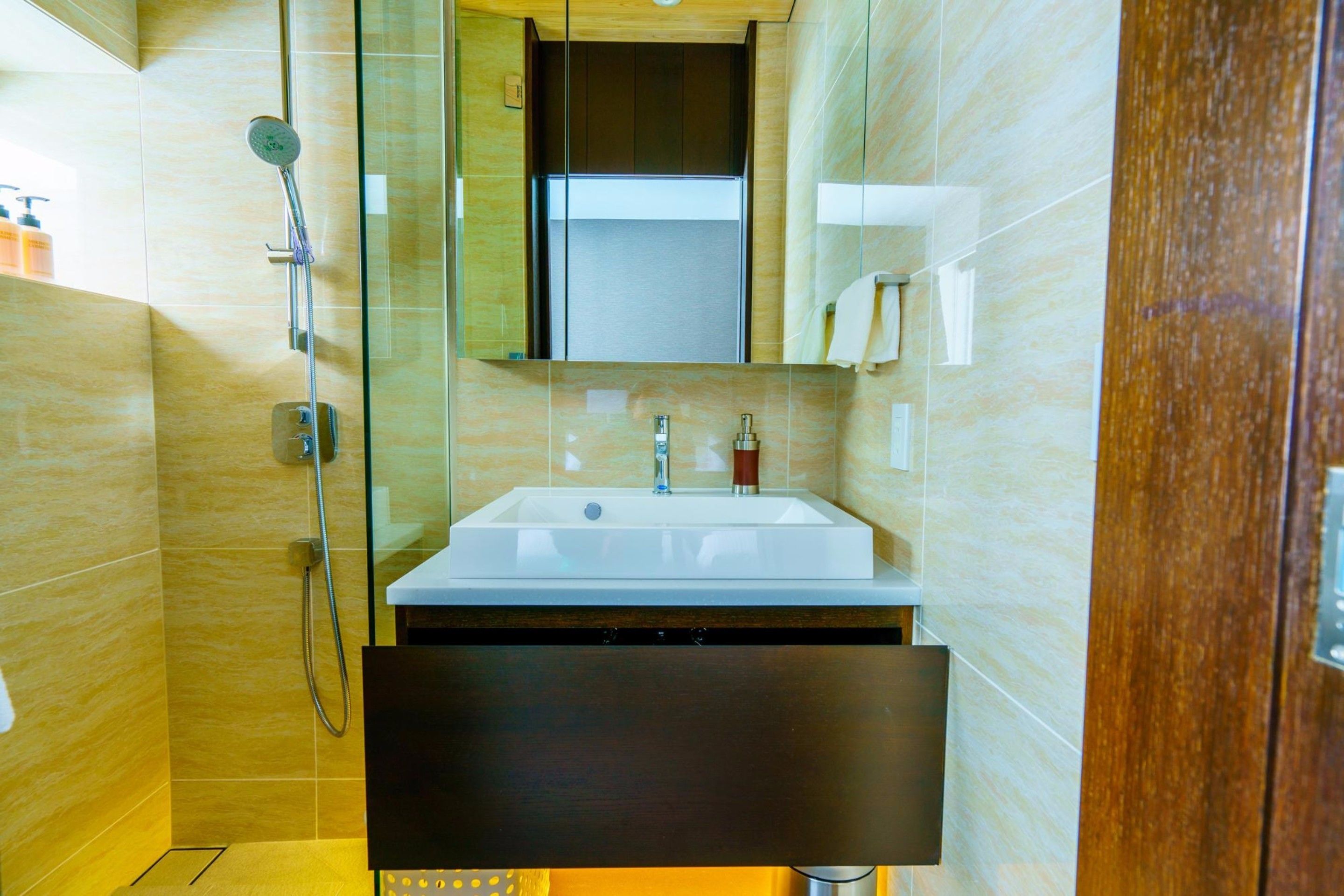 A modern bathroom with a glass-enclosed shower, a white sink, and a wooden cabinet.