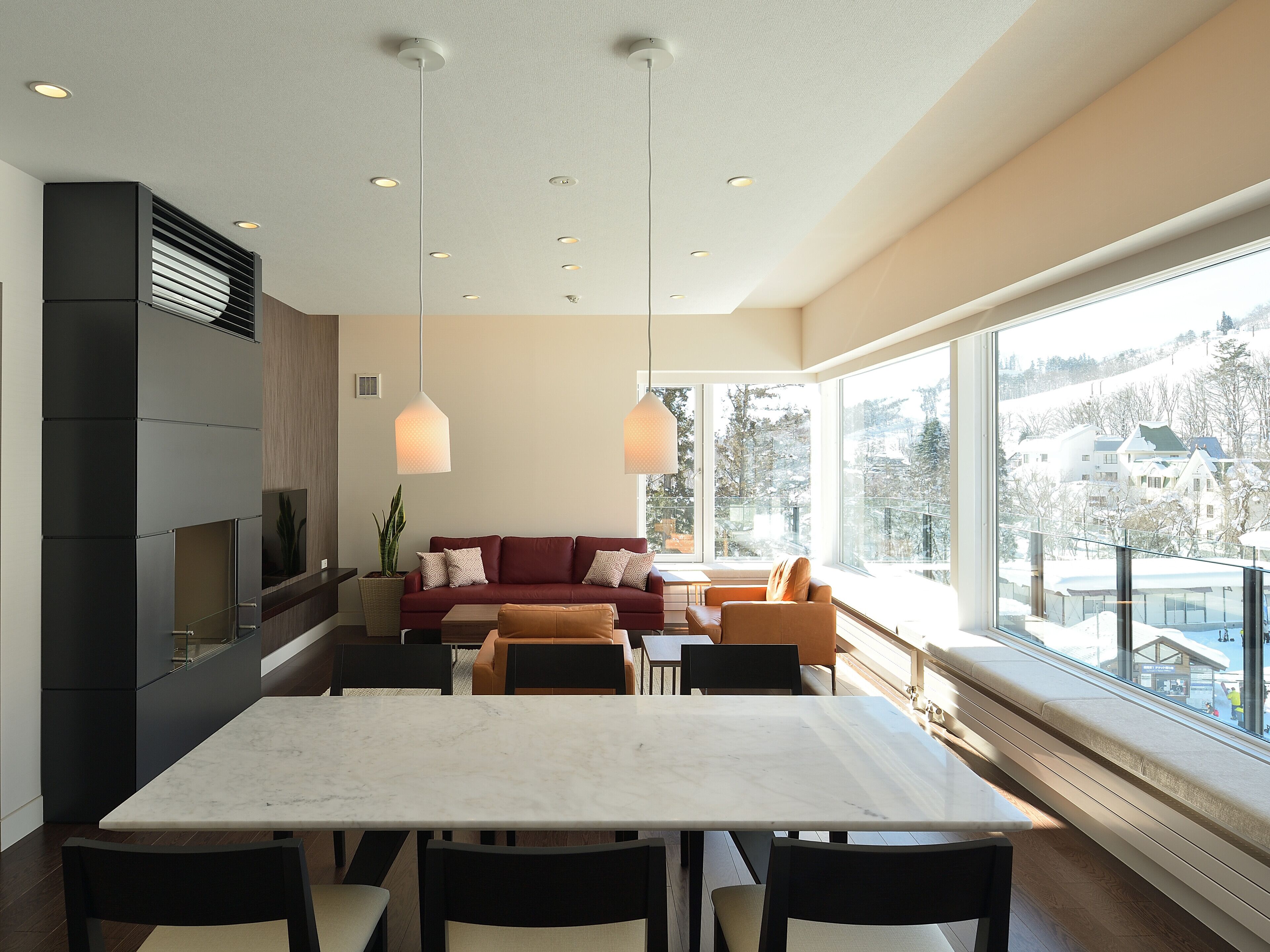 A modern living room with a dining area, large windows, and a view of a snowy landscape.