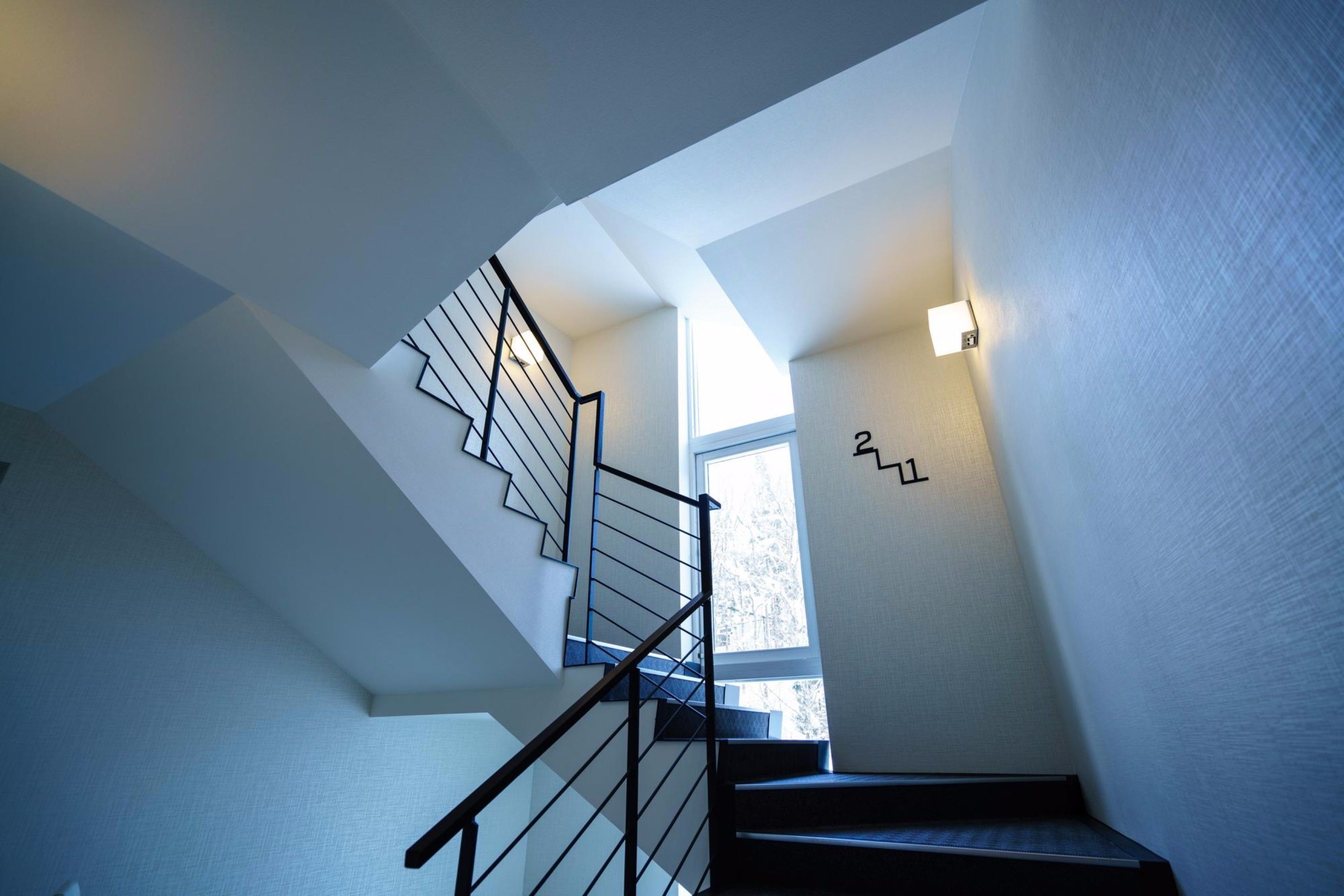 A modern staircase with a glass railing and a light fixture on the wall.