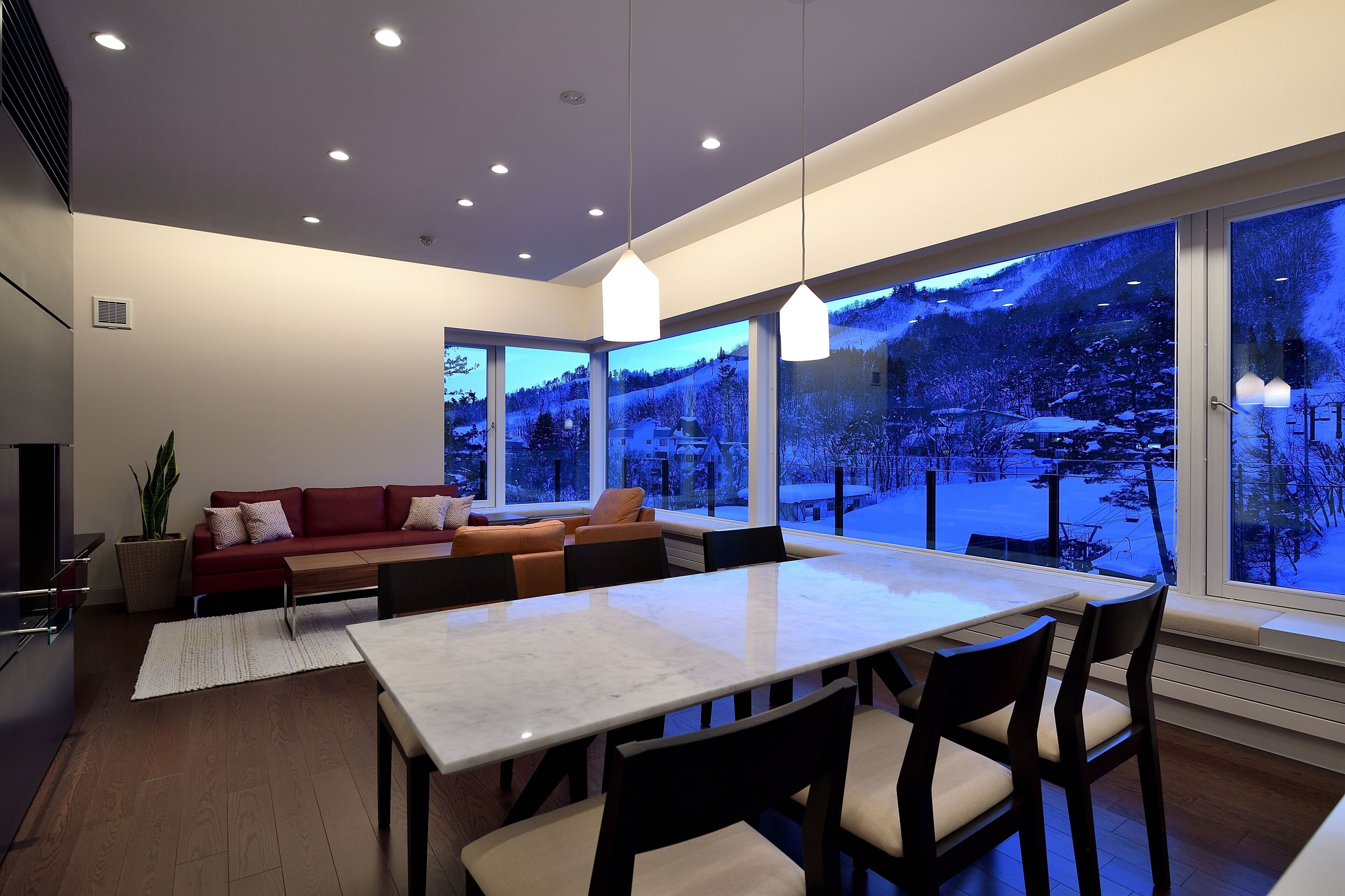 A modern interior with a dining area, a red sofa, and large windows offering a view of a snowy landscape.