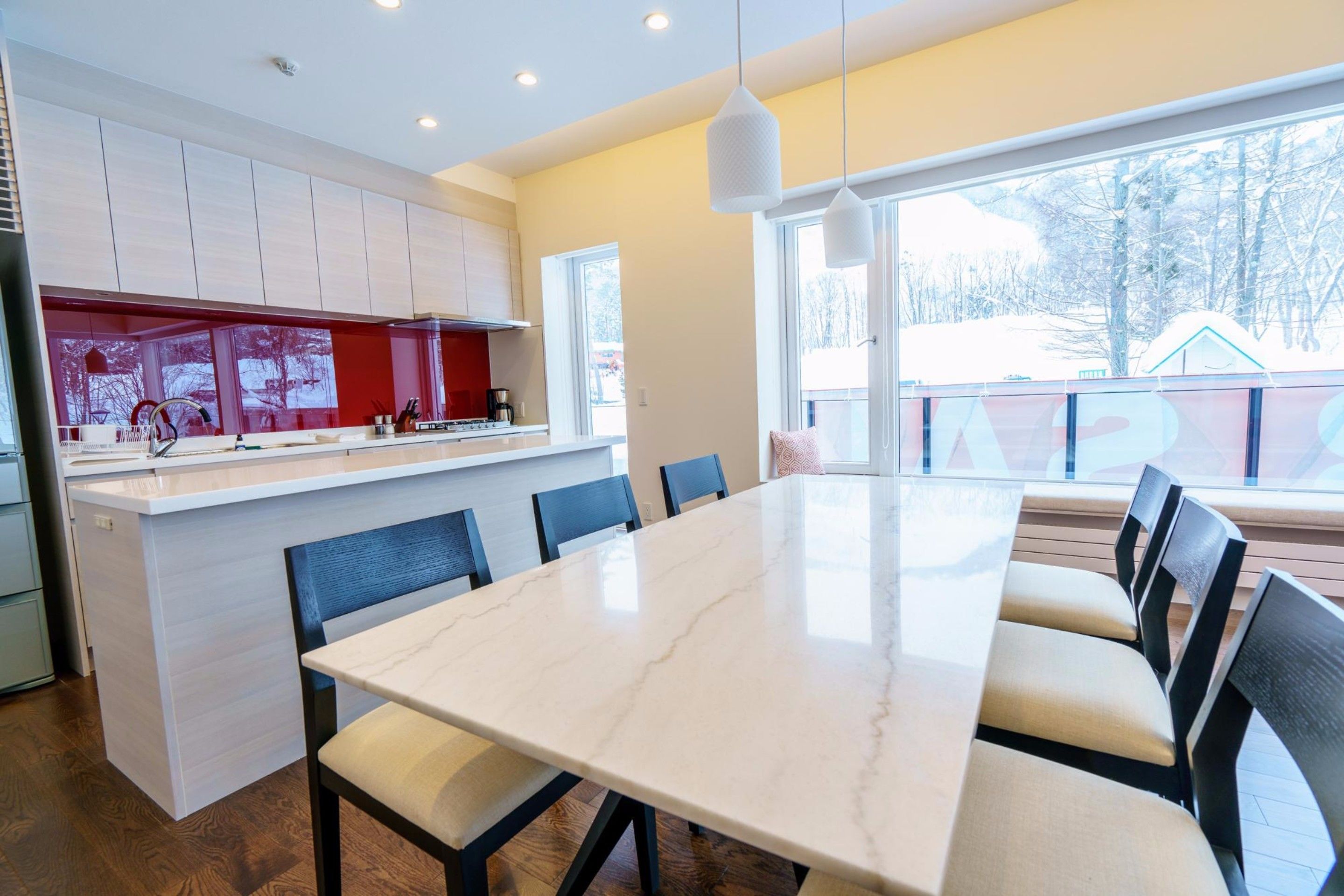 Una cocina moderna con armarios blancos, una isla de mármol y un comedor con una mesa grande y sillas.