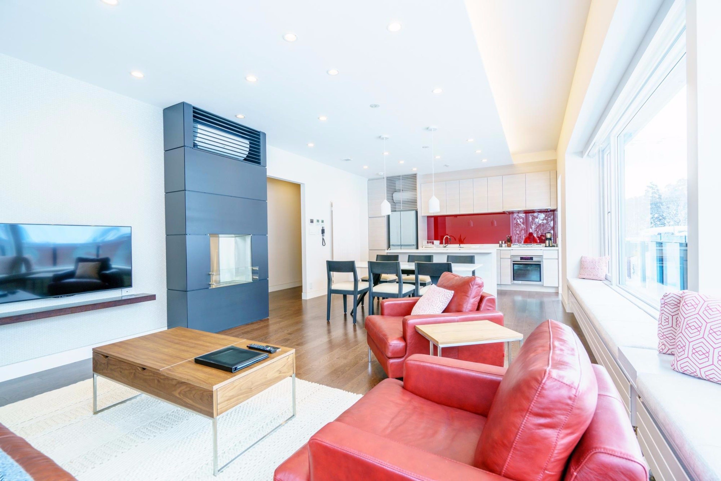 A modern living room with a sofa, coffee table, and TV. There is a kitchen in the background with a dining area.