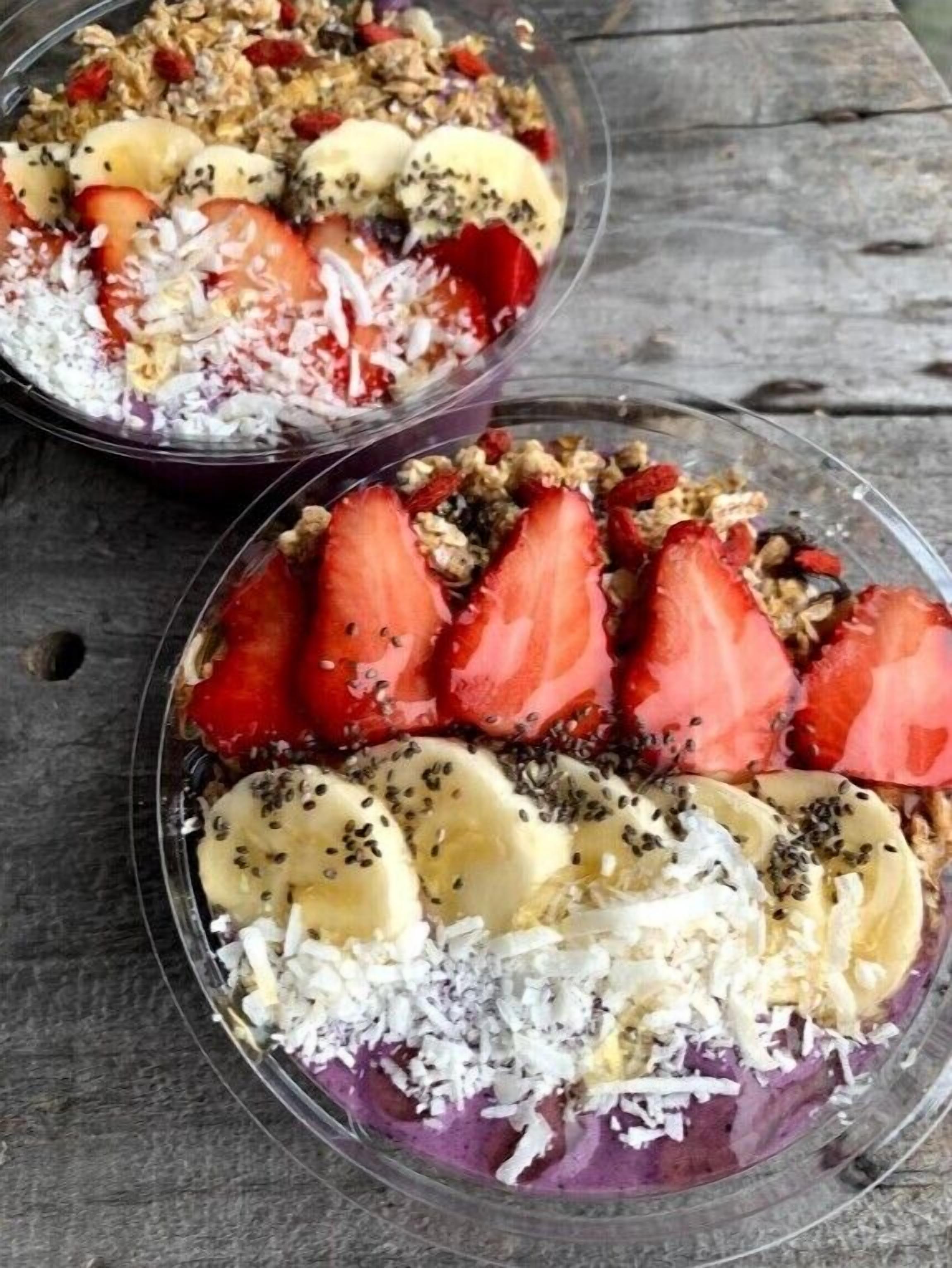 Two bowls of a layered dessert with strawberries, bananas, coconut flakes, and granola.