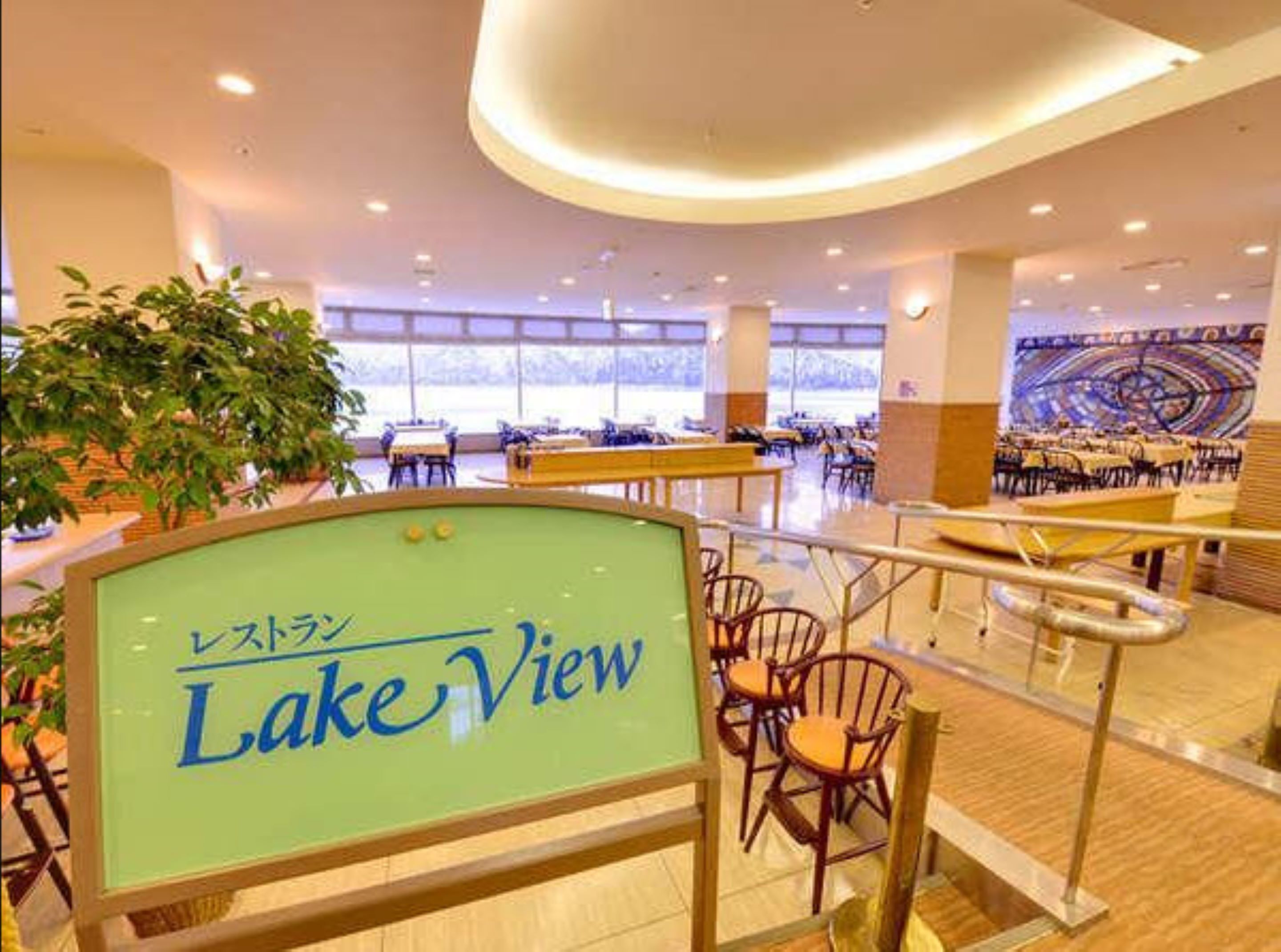 Un espacio interior amplio con varias mesas y sillas, un letrero que dice "Lake View", y un ventanal que ofrece vistas al exterior.