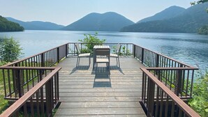 A wooden deck with a table and chairs overlooking a lake with mountains in the background. - Shikaribetsu Lakeside Onsen Hotel Fusui (Shikaoi)