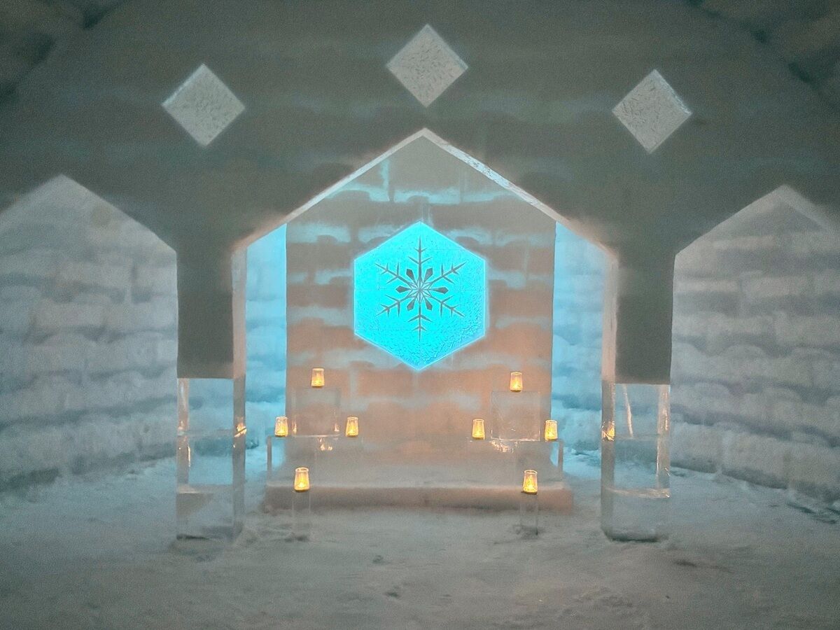 Interno di un hotel di ghiaccio con una scultura di ghiaccio al centro, pareti in ghiaccio e tavoli illuminati da candele.