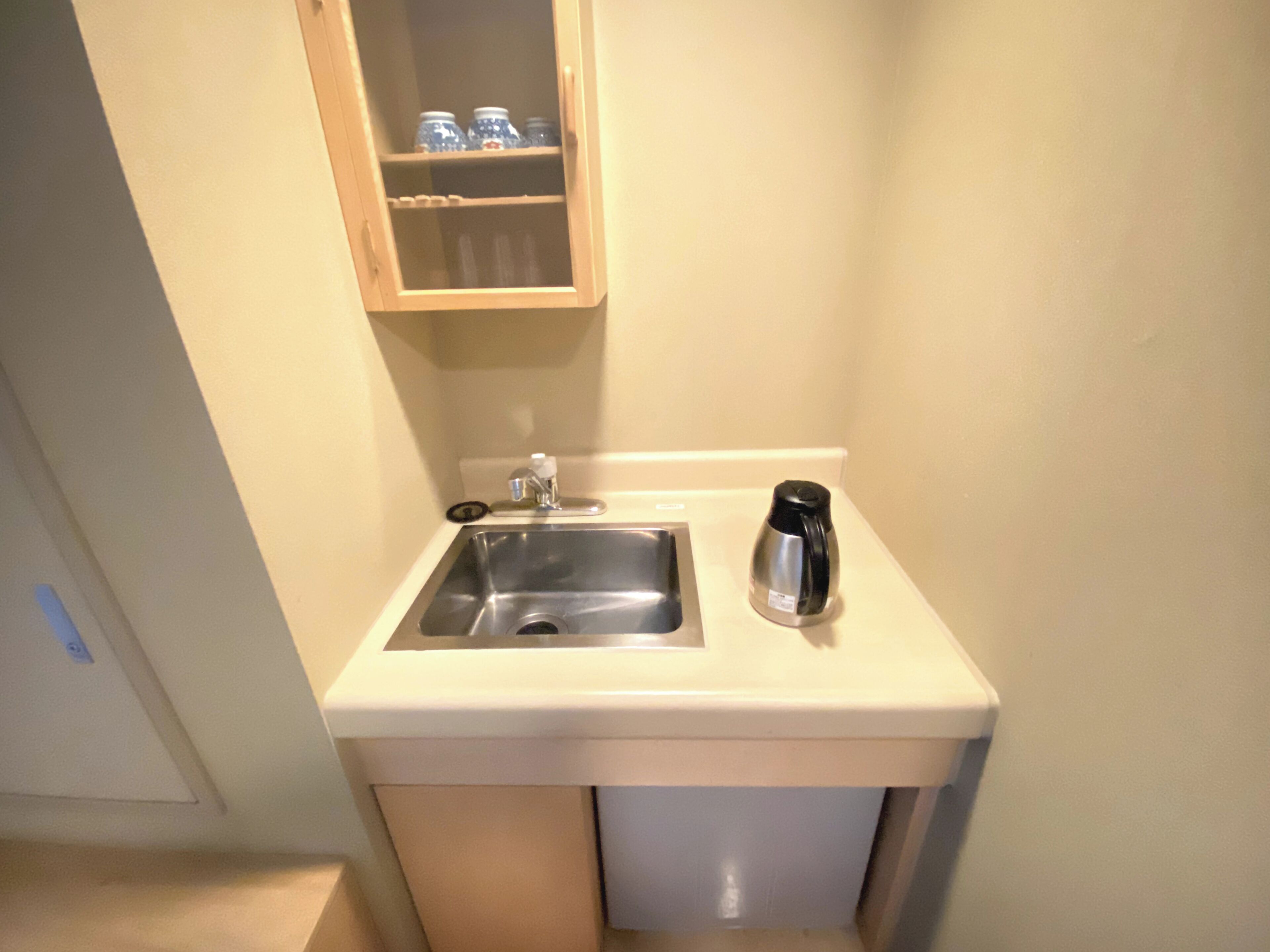 Eine kleine Küche mit Spüle, Kaffeemaschine und einem Schrank über der Spüle.
