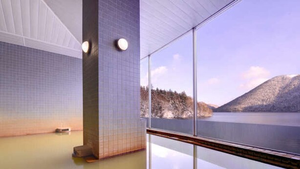 A spa room with a large window offering a view of a lake and mountains. - Shikaribetsu Lakeside Onsen Hotel Fusui (Shikaoi)