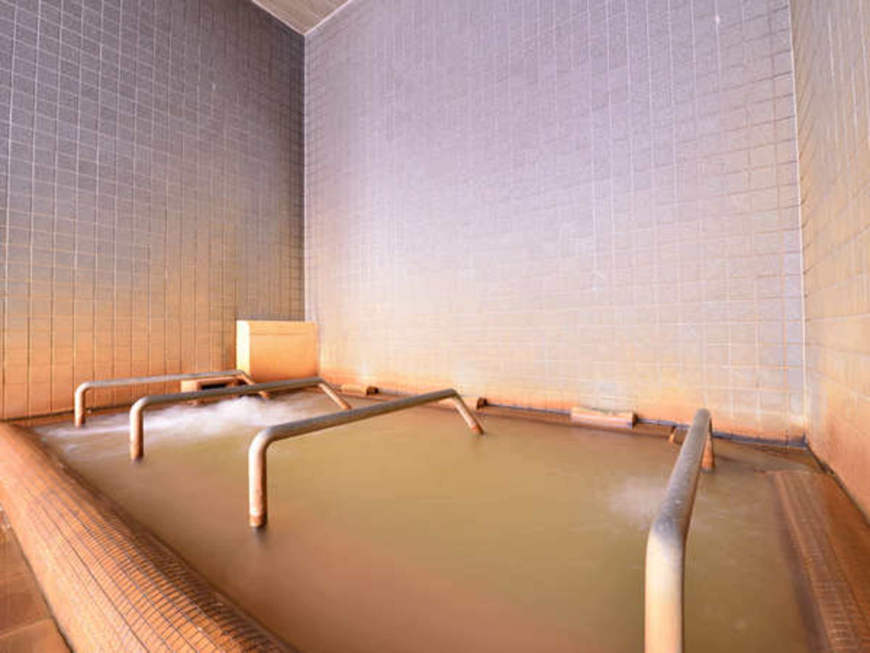 Un bain thermal en plein air, avec des murs recouverts de carreaux et des rampes en métal.