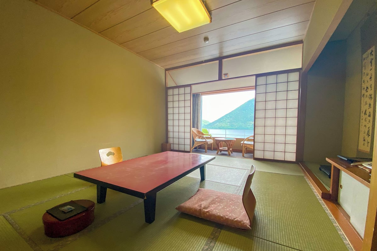 Une pièce de style japonais traditionnel, avec un sol recouvert de tatamis, une table basse et une vue sur une montagne, visible à travers un paravent shoji.