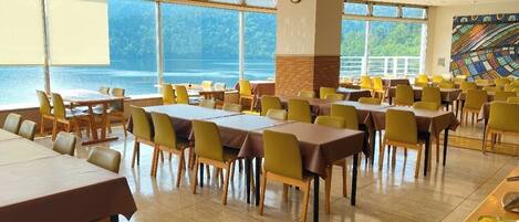 Un amplio comedor con varias mesas y sillas, ventanas grandes que ofrecen vistas al mar y una decoración interior moderna.