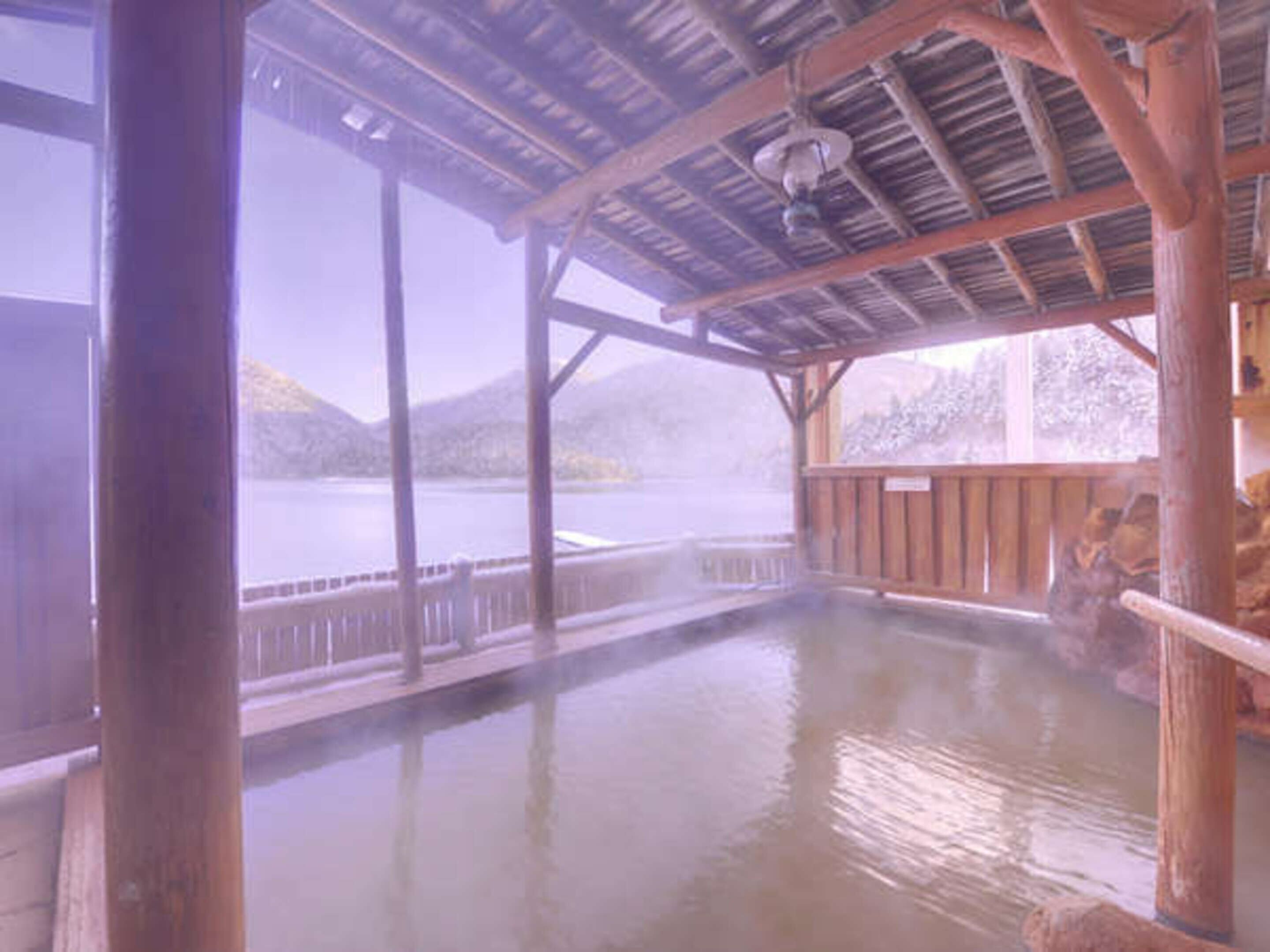 A wooden spa with a hot spring, wooden deck, and a view of a lake and mountains.