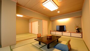 Una habitación tradicional japonesa con suelo de tatami, una mesa baja, un televisor y un armario con un jarrón de flores.