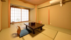 Una habitación tradicional japonesa con suelo de tatami, una mesita baja, un cojín y una puerta corredera que da a un jardín.