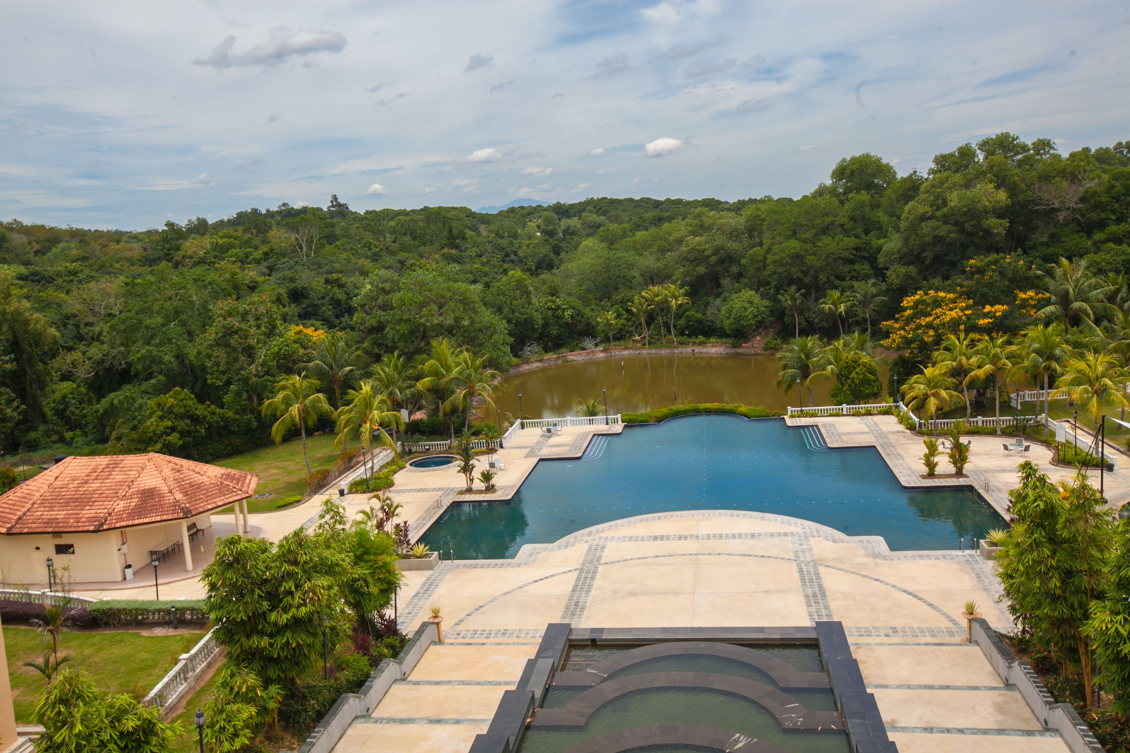 A resort with a large swimming pool surrounded by lush greenery and a small lake.