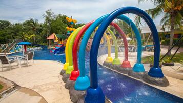 A water park with a pool and slides, surrounded by palm trees and a building with a red roof.
