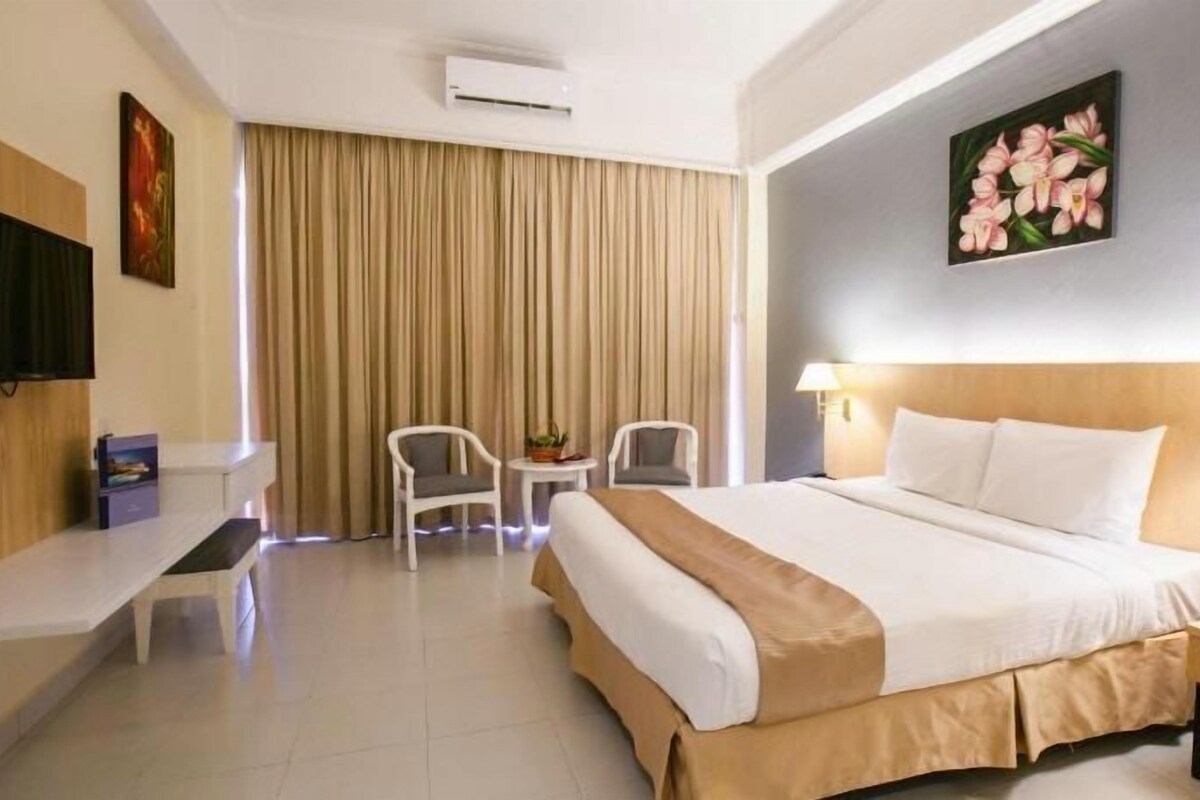 A hotel room with a bed, bedside tables, a desk, a chair, a TV, and a window with curtains.
