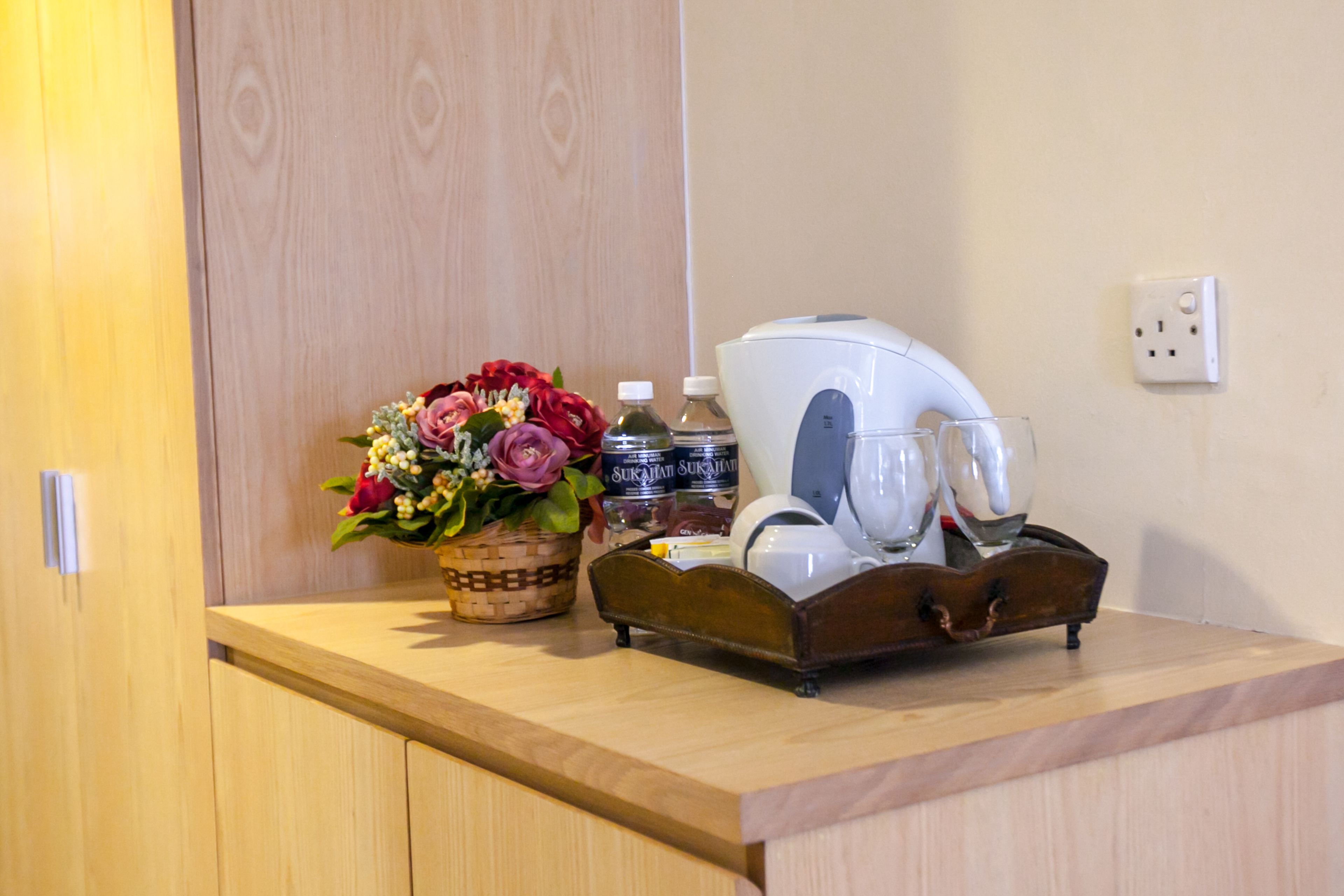 Un comptoir en bois avec un panier de fleurs, une bouteille d’eau, une machine à café et des verres.