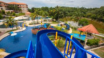 A water park with multiple slides and pools, surrounded by palm trees and a large building in the background.