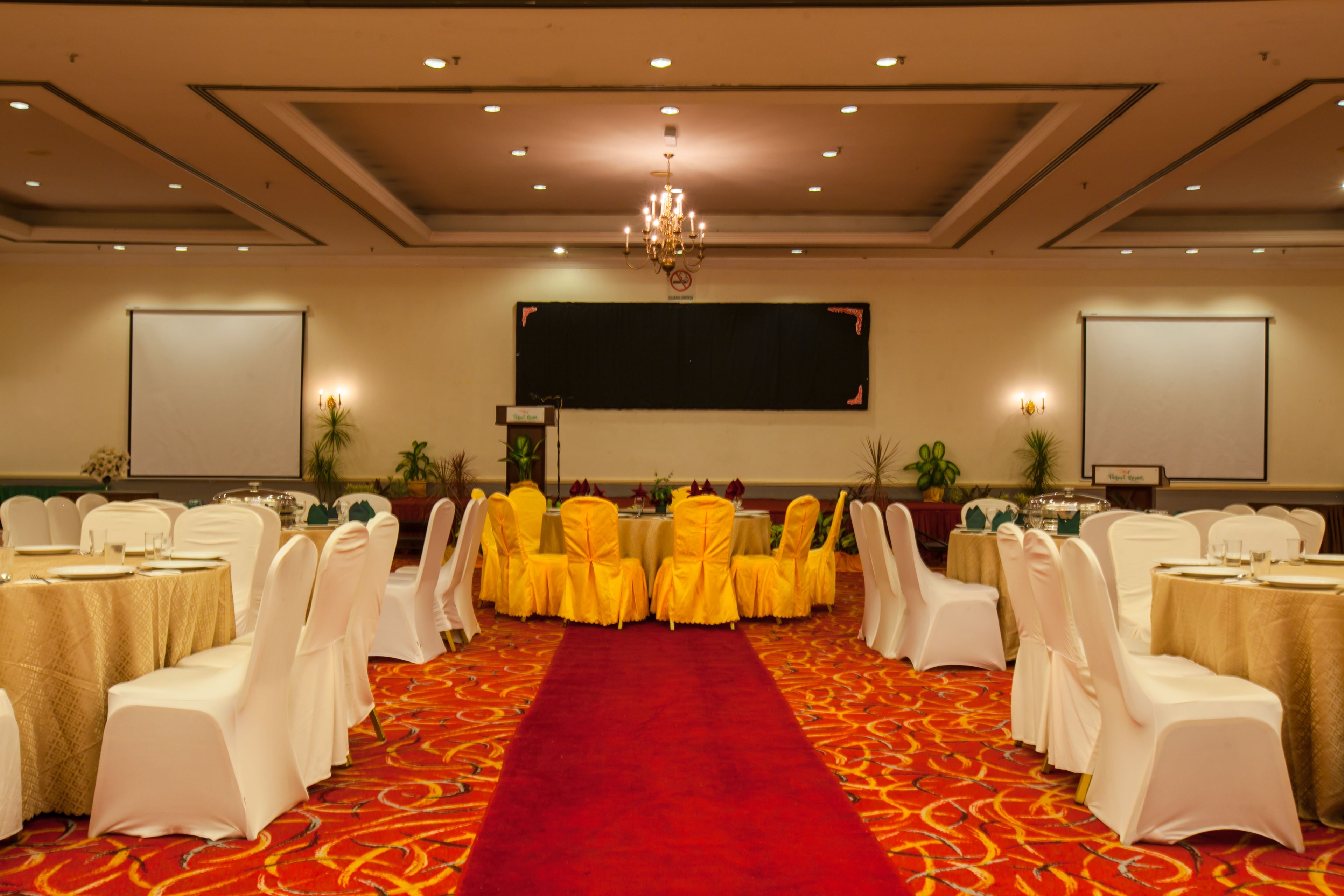 A banquet hall with white chairs, yellow tablecloths, and a red carpet.